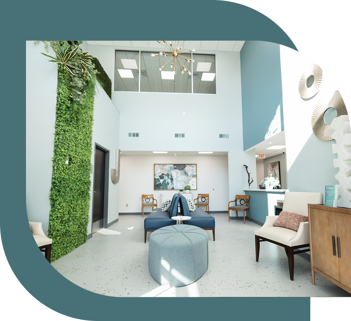 Bright, modern waiting room with tall ceilings, featuring a vertical garden, blue and white chairs, abstract art, and a chandelier. Airy and welcoming.