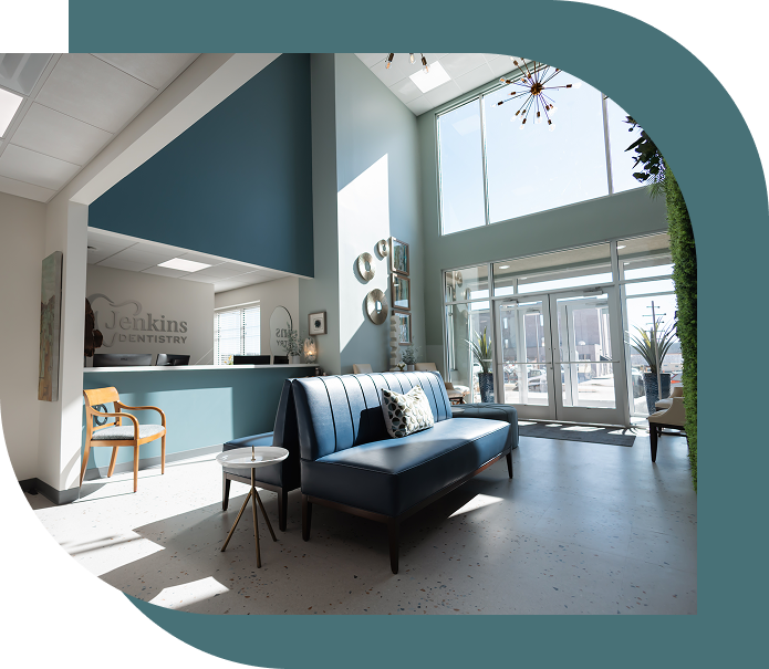 Bright dental office waiting area with high ceilings, large windows, and modern decor. Blue couch, chairs, and wall accents create a welcoming atmosphere.